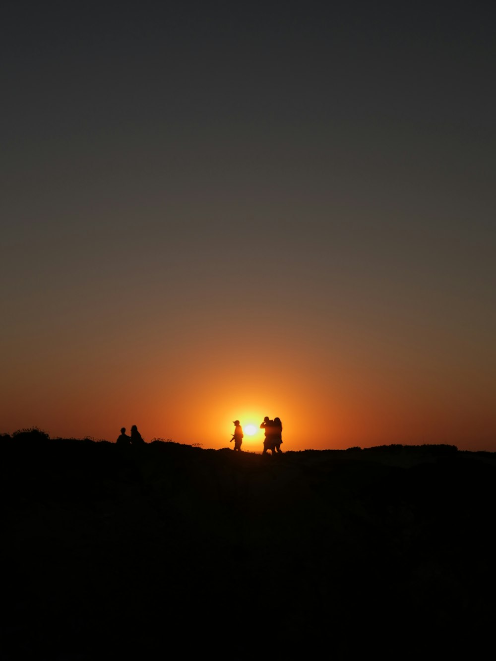 a group of people riding horses across a field at sunset