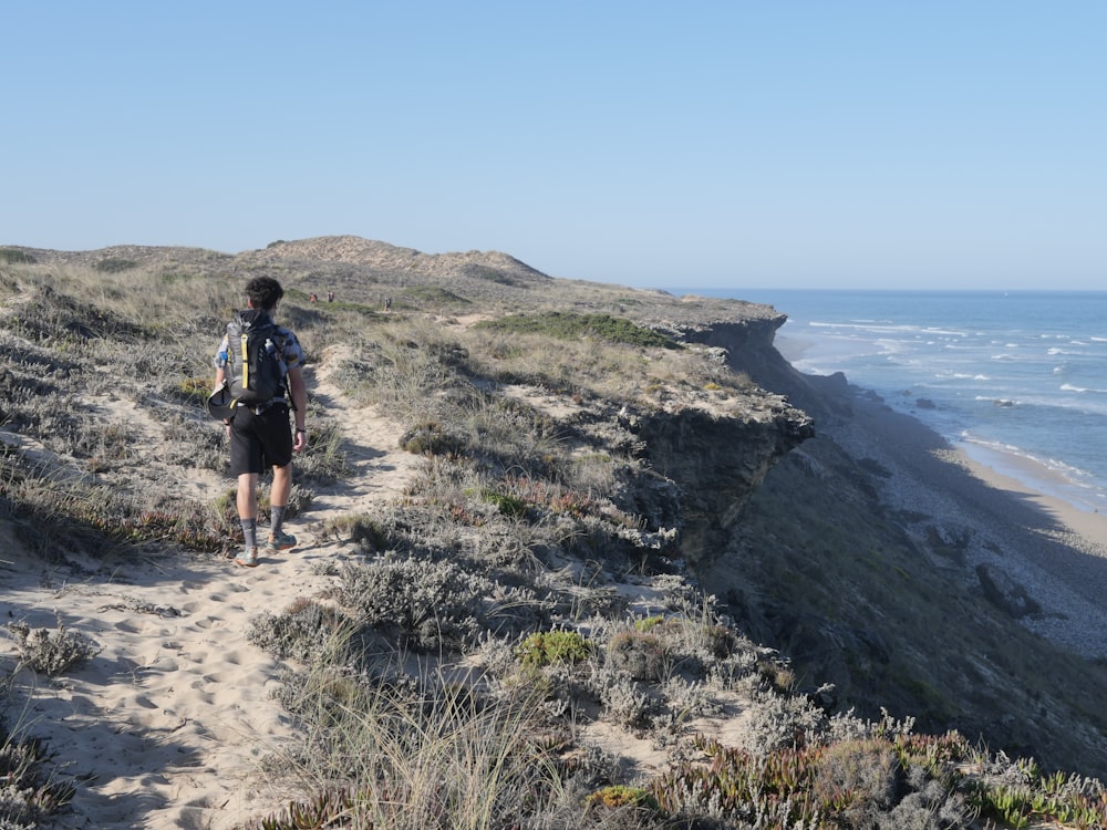 a man walking down a path next to the ocean