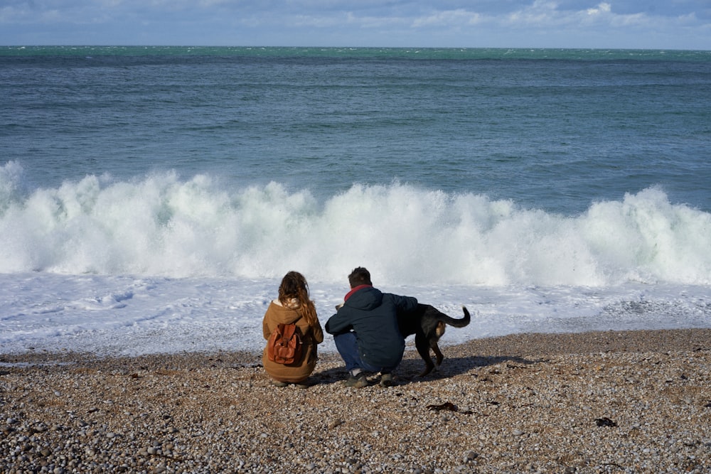 a man and a woman sitting on a beach with a dog