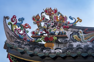 Ornate and colorful carvings feature mythical figures and intricate floral motifs atop a traditional roof structure. The artwork includes vibrant colors and detailed embellishments, showcasing skilled craftsmanship.