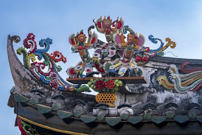 Ornate and colorful carvings feature mythical figures and intricate floral motifs atop a traditional roof structure. The artwork includes vibrant colors and detailed embellishments, showcasing skilled craftsmanship.