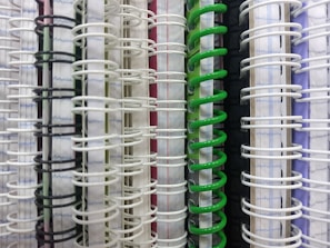A close-up view of several spiral-bound notebooks arranged side by side, showing the spines and coils in various colors including white, black, green, and purple.