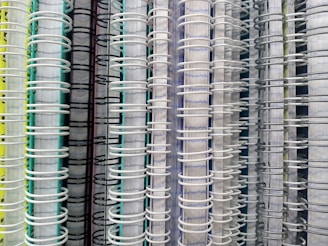 Several spiral-bound notebooks are arranged vertically side by side. The focus is on the spines, which are made of wire binding in various colors, including white, black, and gray. The covers of the notebooks display a range of colors such as yellow, green, and blue.