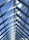 A series of triangular glass panels form a modern, symmetric roof structure. The panels allow natural light to stream through, and the clear blue sky is visible beyond. Metal framing holds the glass panes in place, creating a clean and geometric pattern accented by cables.