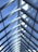 A series of triangular glass panels form a modern, symmetric roof structure. The panels allow natural light to stream through, and the clear blue sky is visible beyond. Metal framing holds the glass panes in place, creating a clean and geometric pattern accented by cables.