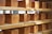Several loaves of bread are neatly arranged on wooden shelves. The loaves are uniformly shaped and have a golden-brown crust. Some natural light seems to be entering from a window in the background, illuminating the loaves.