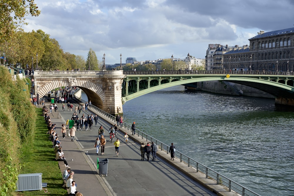 a group of people walking down a sidewalk next to a river