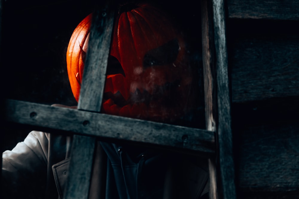 uma pessoa usando uma assustadora máscara de abóbora em uma janela