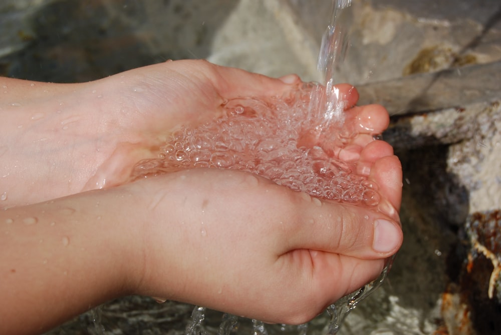 a person's hand holding a water faucet over a stream of water