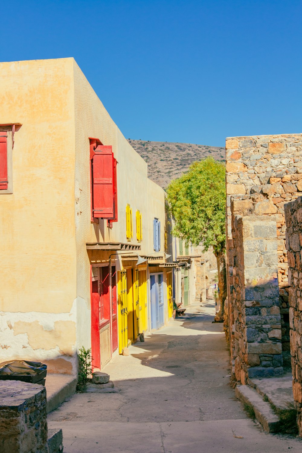 a narrow street with a yellow building and red shutters