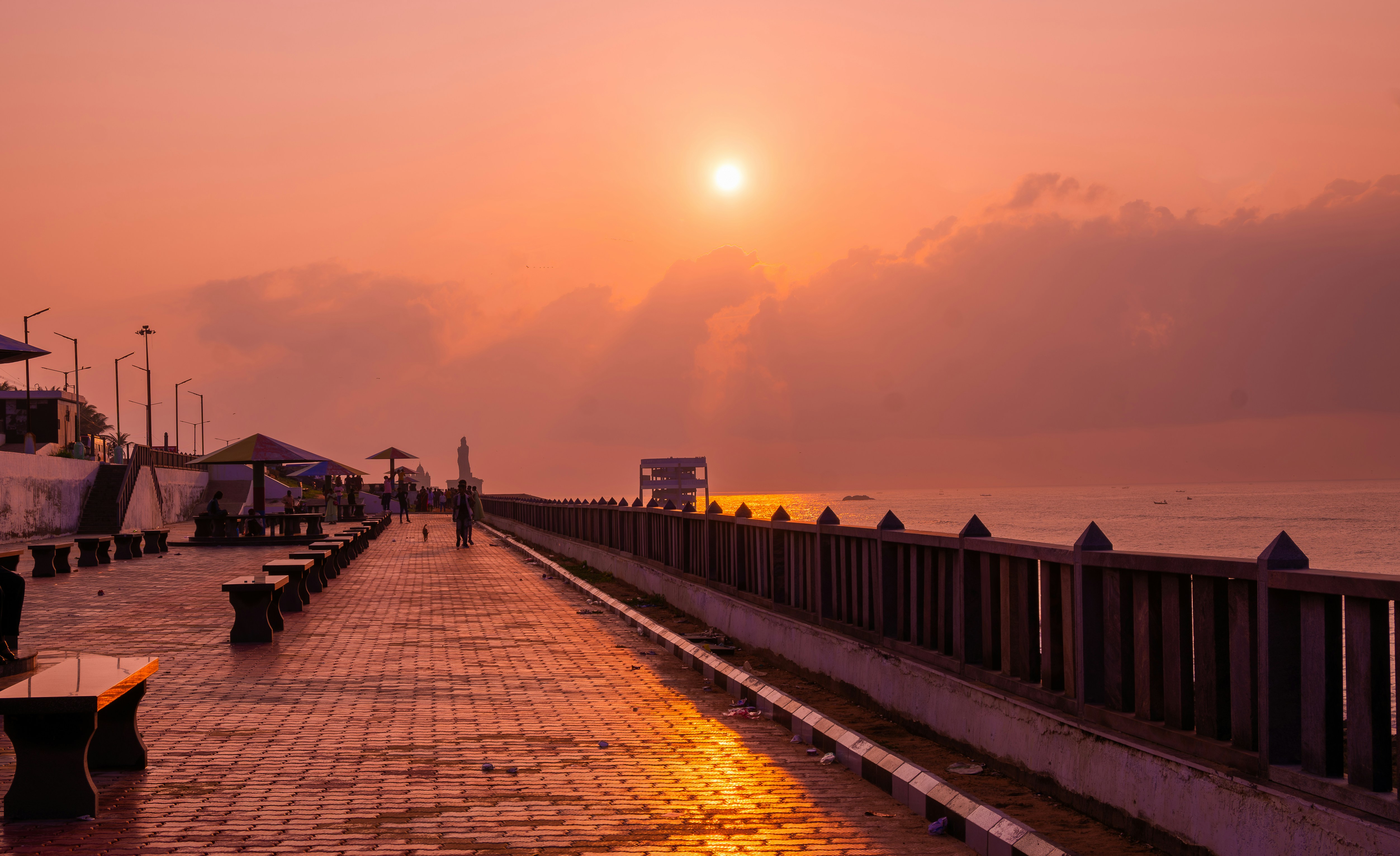 the sun is setting over the ocean with benches and umbrellas