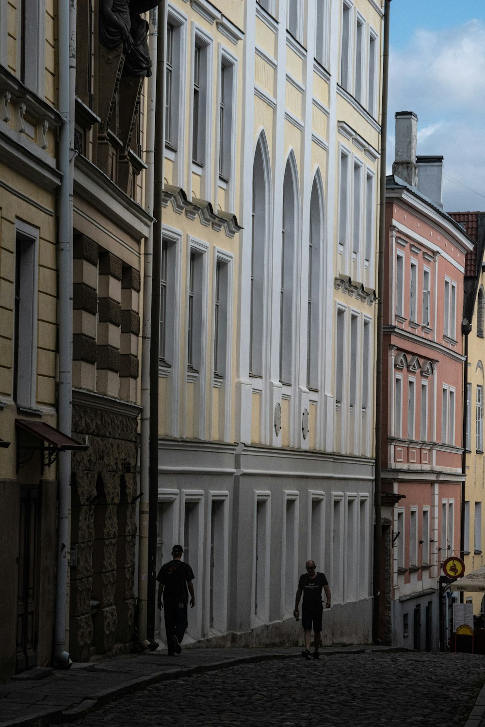 a couple of people walking down a street next to tall buildings