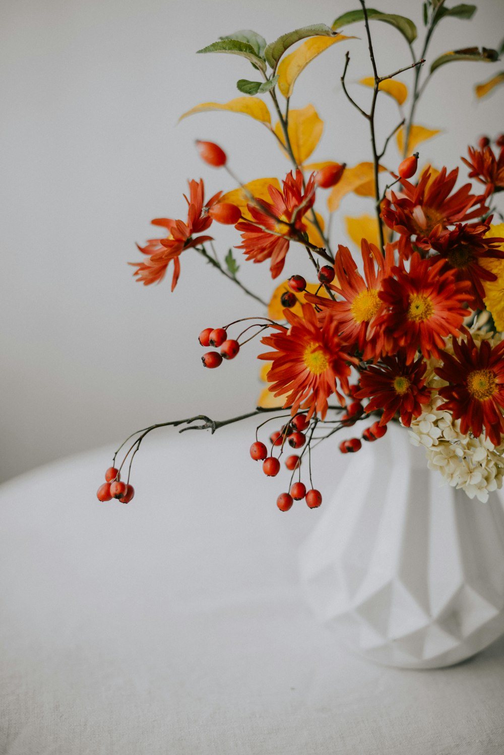a white vase filled with red and yellow flowers