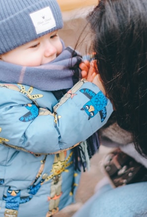 A playful parent and child wearing matching knit scarves, smiling outdoors in winter.