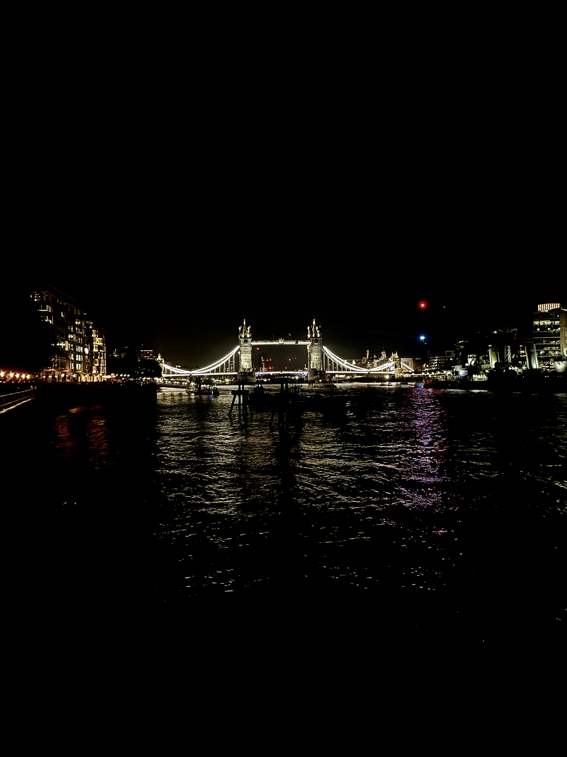 A vibrant shot of a classic London black cab cruising past the illuminated Tower Bridge at dusk, with the bridge's lights reflecting on the Thames.