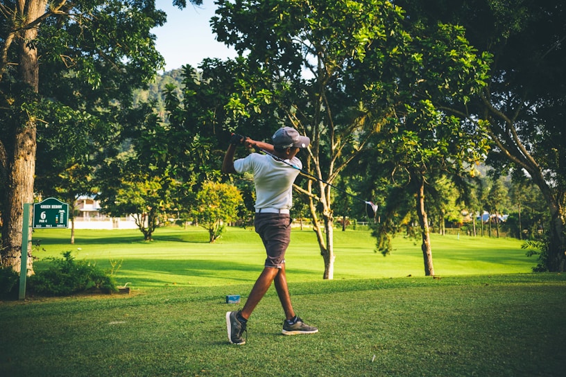 A sunlit fairway stretching out with a golfer mid-swing, surrounded by lush greenery.