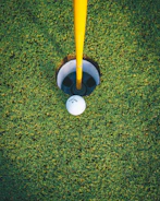 Close-up of a golf ball resting on the edge of a hole.