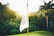 A sunlit golf course with lush green grass is depicted, featuring a flagpole with a flag labeled 'St Andrews Golf Club.' The flag is highlighted by the warm glow of the setting or rising sun, casting soft light over the surrounding trees and plants.