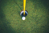 Close-up shot of a golf ball resting on the green near the hole with a flag fluttering in the breeze.