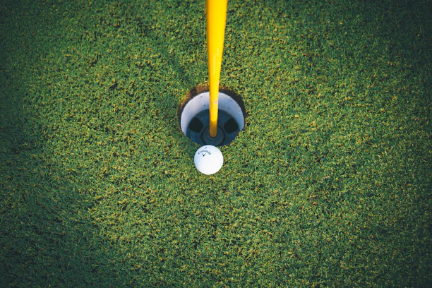 Close-up of a golf ball resting on the green near the hole under a clear blue sky.