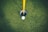 A golf ball rests near the edge of a hole on a neatly trimmed green. The yellow flagpole stands upright, indicating the location of the hole. The grass appears lush and well-maintained, providing a rich green backdrop.