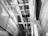 An interior view of an elevator shaft showing cables, metal beams, and structural components. The perspective is angular, focusing on the vertical lines and intricate machinery.