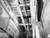 An interior view of an elevator shaft showing cables, metal beams, and structural components. The perspective is angular, focusing on the vertical lines and intricate machinery.
