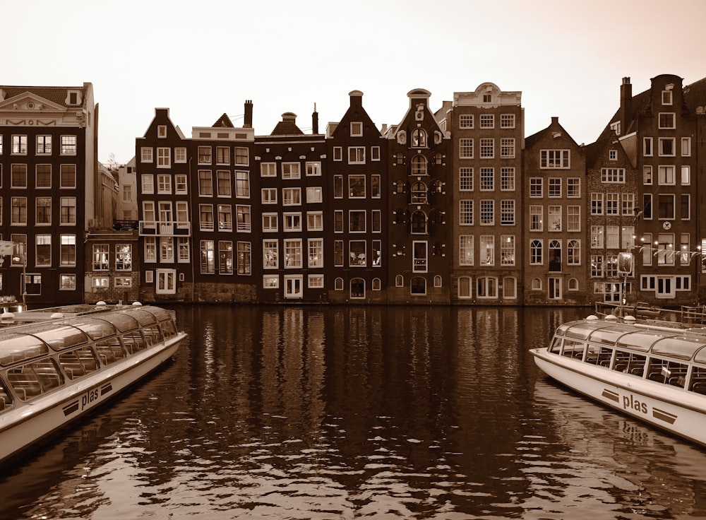 a group of boats floating on top of a river next to tall buildings