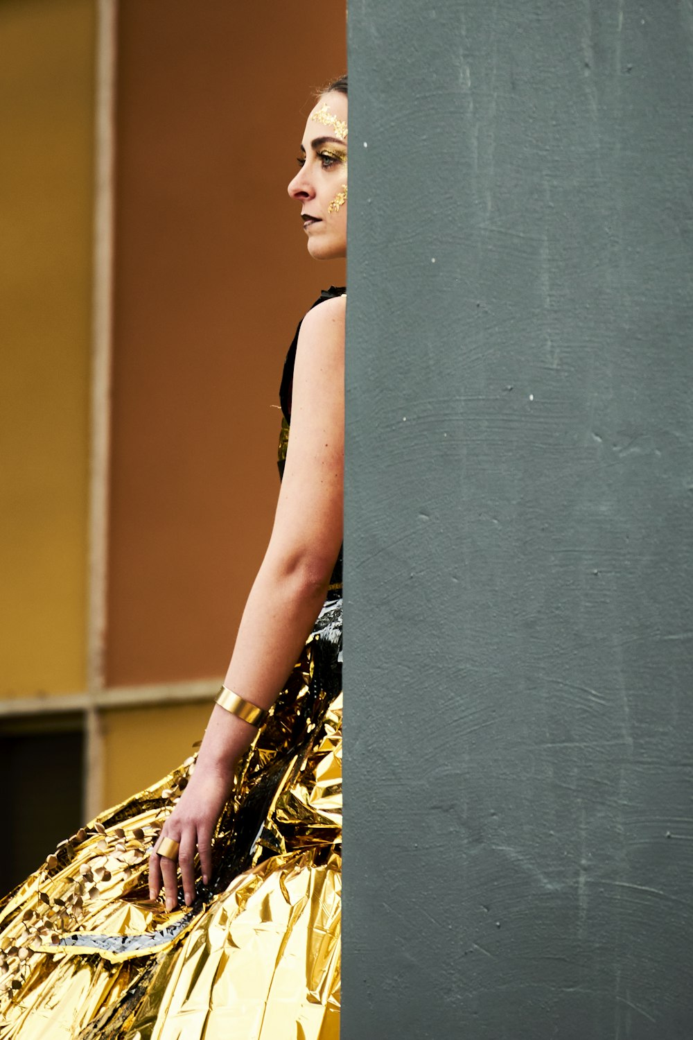 a woman in a gold dress leaning against a wall