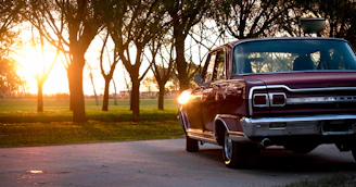 A vintage car parked beside a rustic wooden fence under warm sunset light.