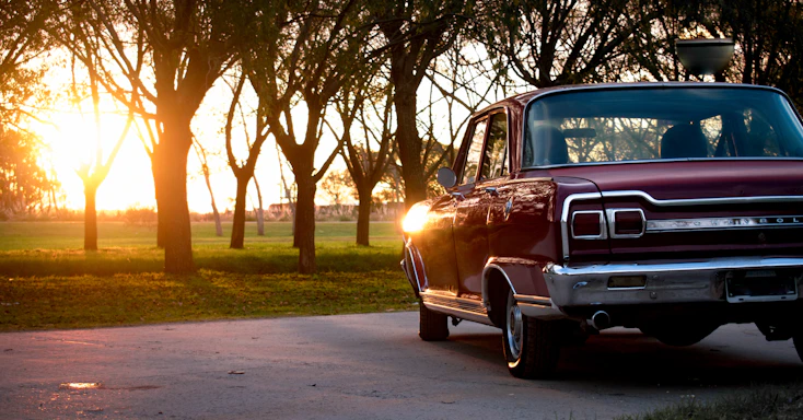 A vintage car parked beside a rustic wooden fence under warm sunset light.