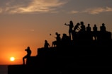 A group of photographers gathered on a rocky coastline during sunset, cameras ready.
