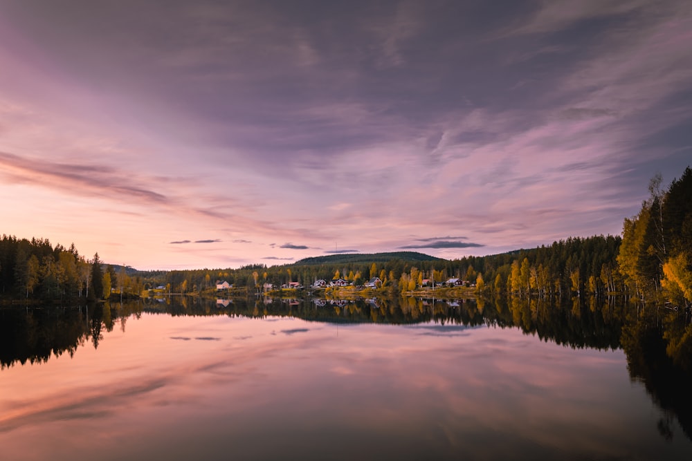 a lake surrounded by trees with a sunset in the background