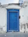 Before-and-after images showing a damaged door replaced and newly painted, framed by white trim and blue siding.