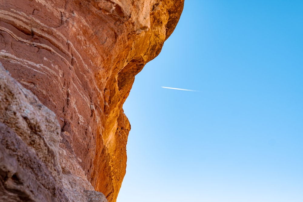 a plane flying in the sky over a rocky cliff