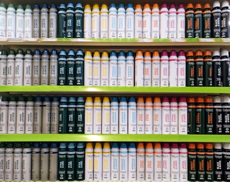 Several shelves in a store displaying neatly organized bottles of various personal care products. The bottles come in different colors and are arranged by type and purpose, with labels clearly visible. The shelves are green, and the organization gives a sense of order and cleanliness.