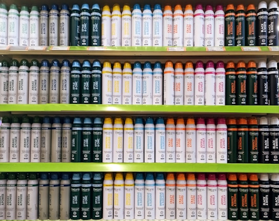 Several shelves in a store displaying neatly organized bottles of various personal care products. The bottles come in different colors and are arranged by type and purpose, with labels clearly visible. The shelves are green, and the organization gives a sense of order and cleanliness.