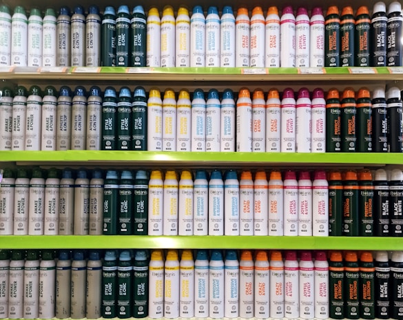 Several shelves in a store displaying neatly organized bottles of various personal care products. The bottles come in different colors and are arranged by type and purpose, with labels clearly visible. The shelves are green, and the organization gives a sense of order and cleanliness.