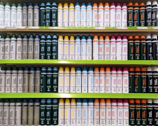 Several shelves in a store displaying neatly organized bottles of various personal care products. The bottles come in different colors and are arranged by type and purpose, with labels clearly visible. The shelves are green, and the organization gives a sense of order and cleanliness.