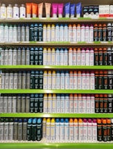 Rows of shelves filled with various colorful bottles and tubes, including creams and sprays. The products are neatly arranged in an orderly display, showcasing different brands and types, each with distinctive colored labels and caps.