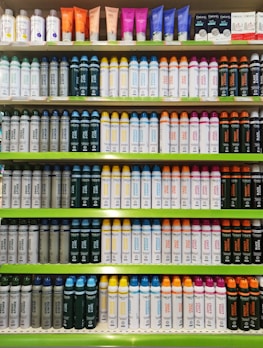Rows of shelves filled with various colorful bottles and tubes, including creams and sprays. The products are neatly arranged in an orderly display, showcasing different brands and types, each with distinctive colored labels and caps.