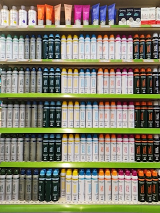 Rows of shelves filled with various colorful bottles and tubes, including creams and sprays. The products are neatly arranged in an orderly display, showcasing different brands and types, each with distinctive colored labels and caps.
