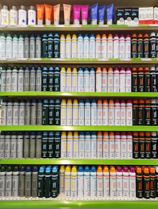 Rows of shelves filled with various colorful bottles and tubes, including creams and sprays. The products are neatly arranged in an orderly display, showcasing different brands and types, each with distinctive colored labels and caps.