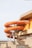 An orange spiral water slide is attached to the exterior of a building, supported by grey metal beams. The building has a brutalist architectural style with concrete surfaces and angular shapes. The slide twists and turns downwards, casting shadows on the structure.