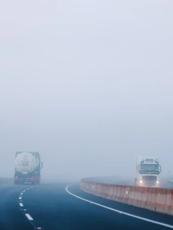 a couple of trucks driving down a foggy road