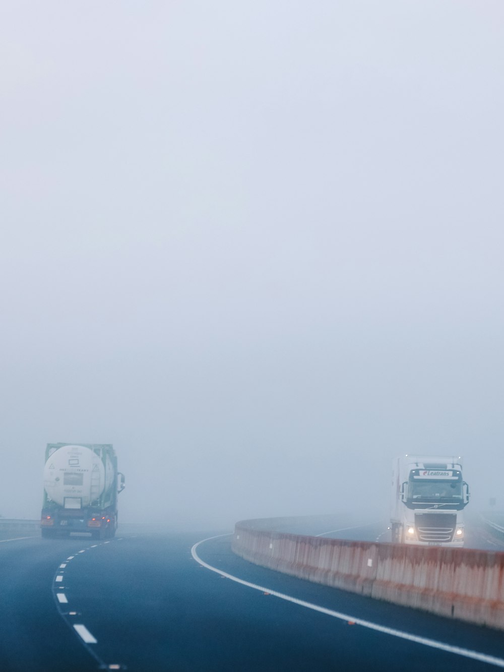 a couple of trucks driving down a foggy road