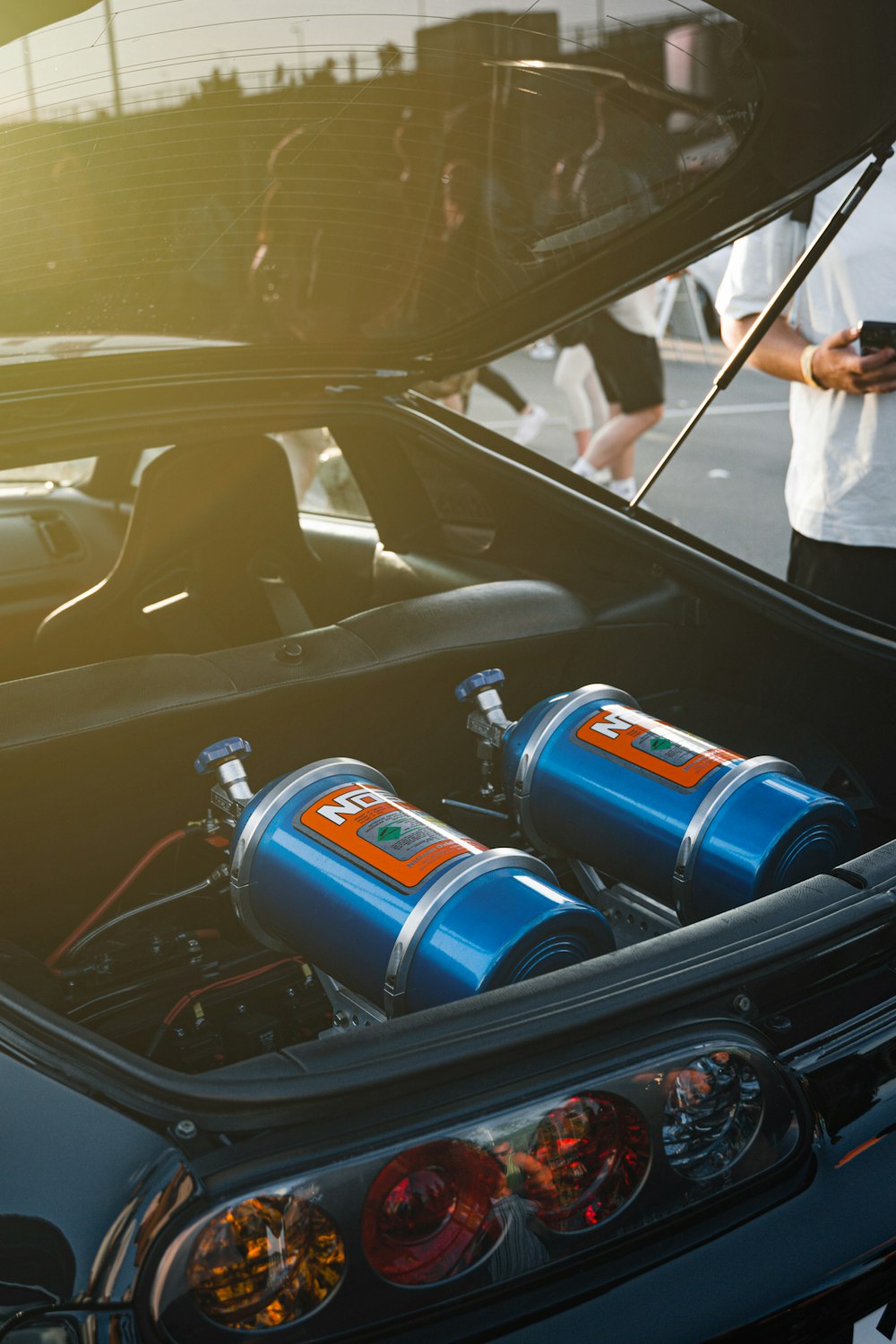 a car with a hood open and two blue canisters in the trunk
