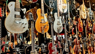 A collection of electric guitars displayed vertically on a wall, showcasing various designs, colors, and finishes. The guitars range from shiny metallic to wooden textures, with intricate details and hardware visible.