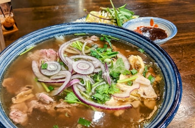 A vibrant bowl of steaming Vietnamese pho with fresh herbs and lime.