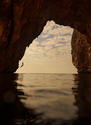 a person standing in the water in front of a cave